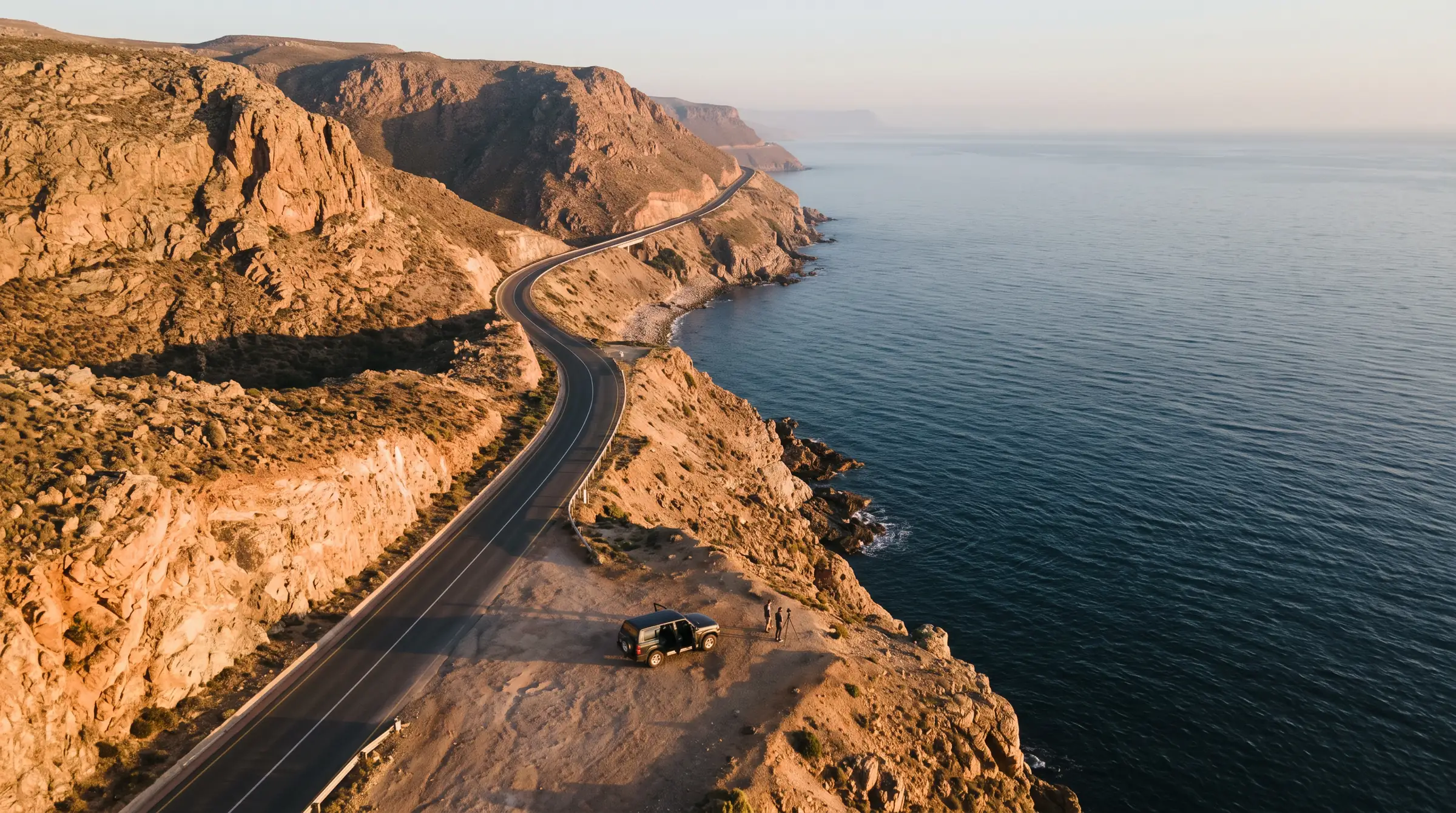 Aerial view of a winding coastal road above the sea at sunrise